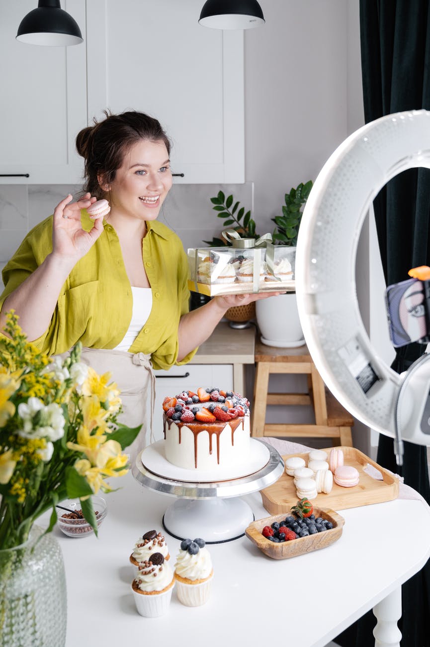 smiling woman showing assorted yummy homemade cakes while recording vlog